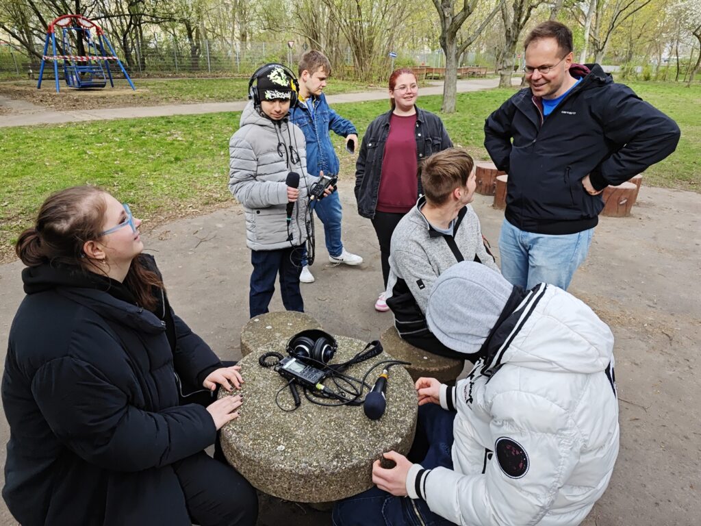 Schüler und Schülerinnen und ein Lehrer auf dem Schulhof mit Aufnahmegeräten